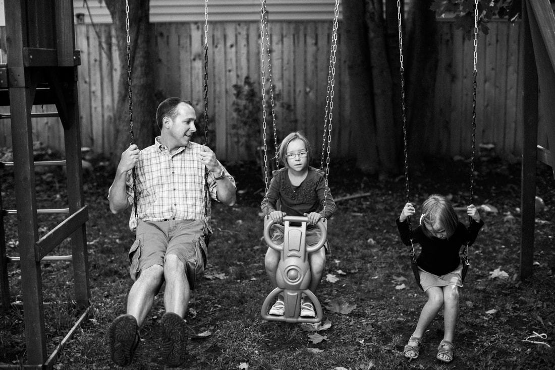 family photograph of father and two daughters on swing set